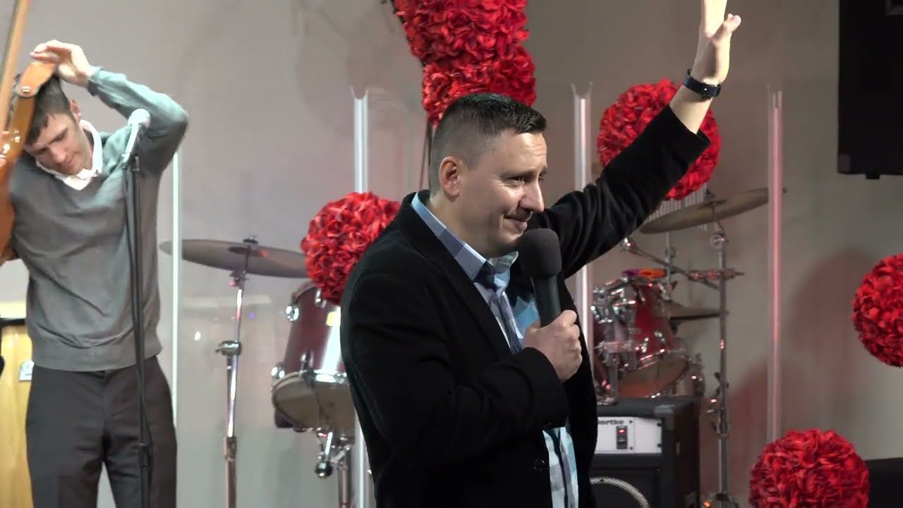 Ruslan Murin holding a microphone and raising one arm, with a man holding a guitar behind him.