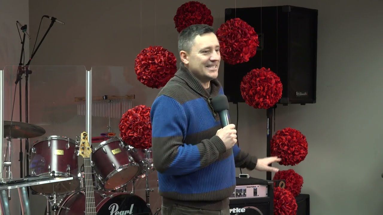 Ruslan Murin in a striped sweater smiling and holding a microphone, with drums behind him.