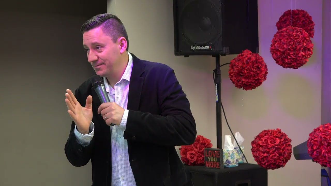 Ruslan Murin in a dark jacket preaching into a microphone and gesturing with an open hand.