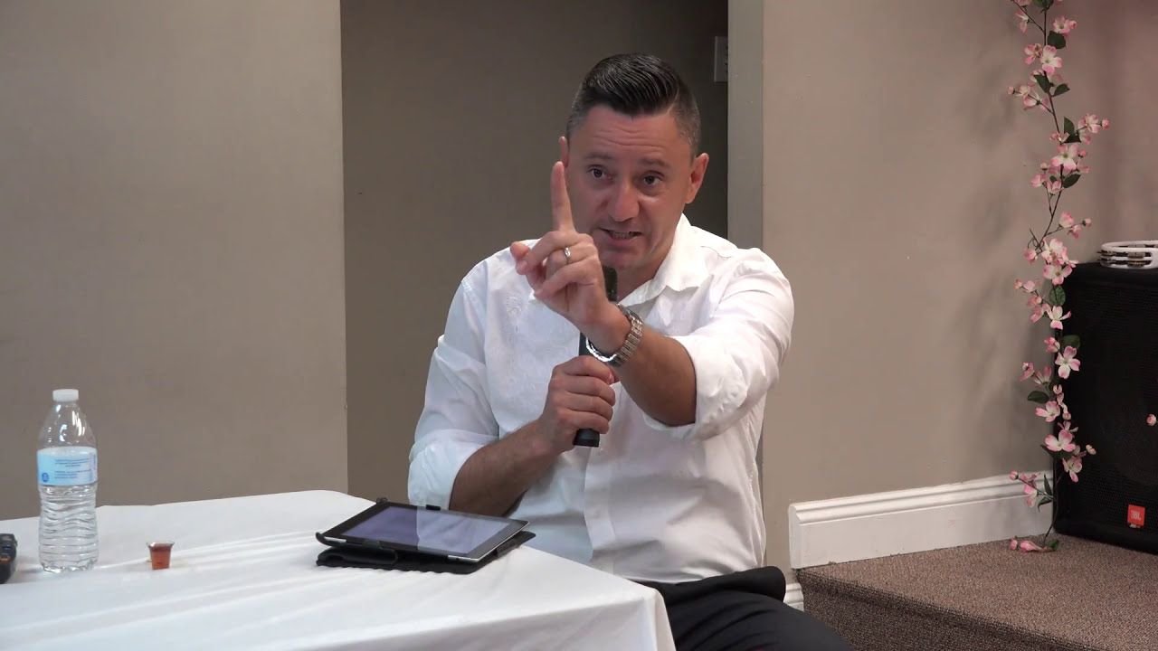 Ruslan Murin seated at a table with a microphone, raising his index finger.