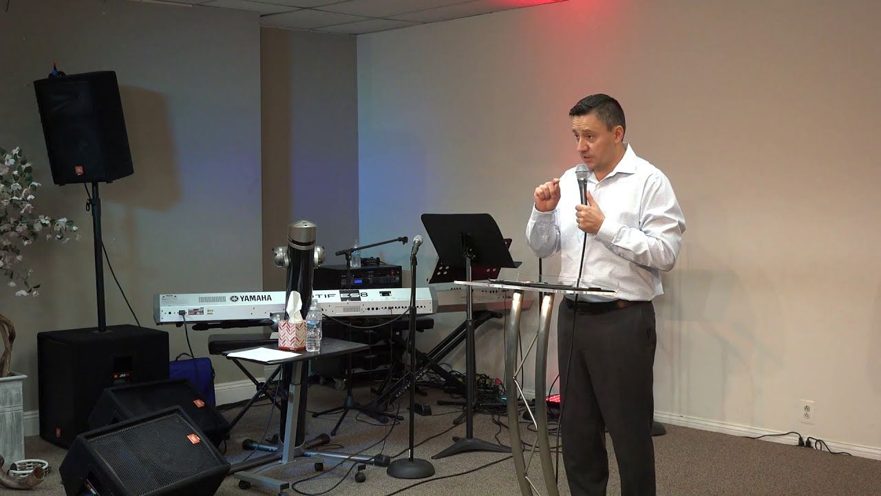 Ruslan Murin in a white shirt preaching into a microphone at a clear lectern.