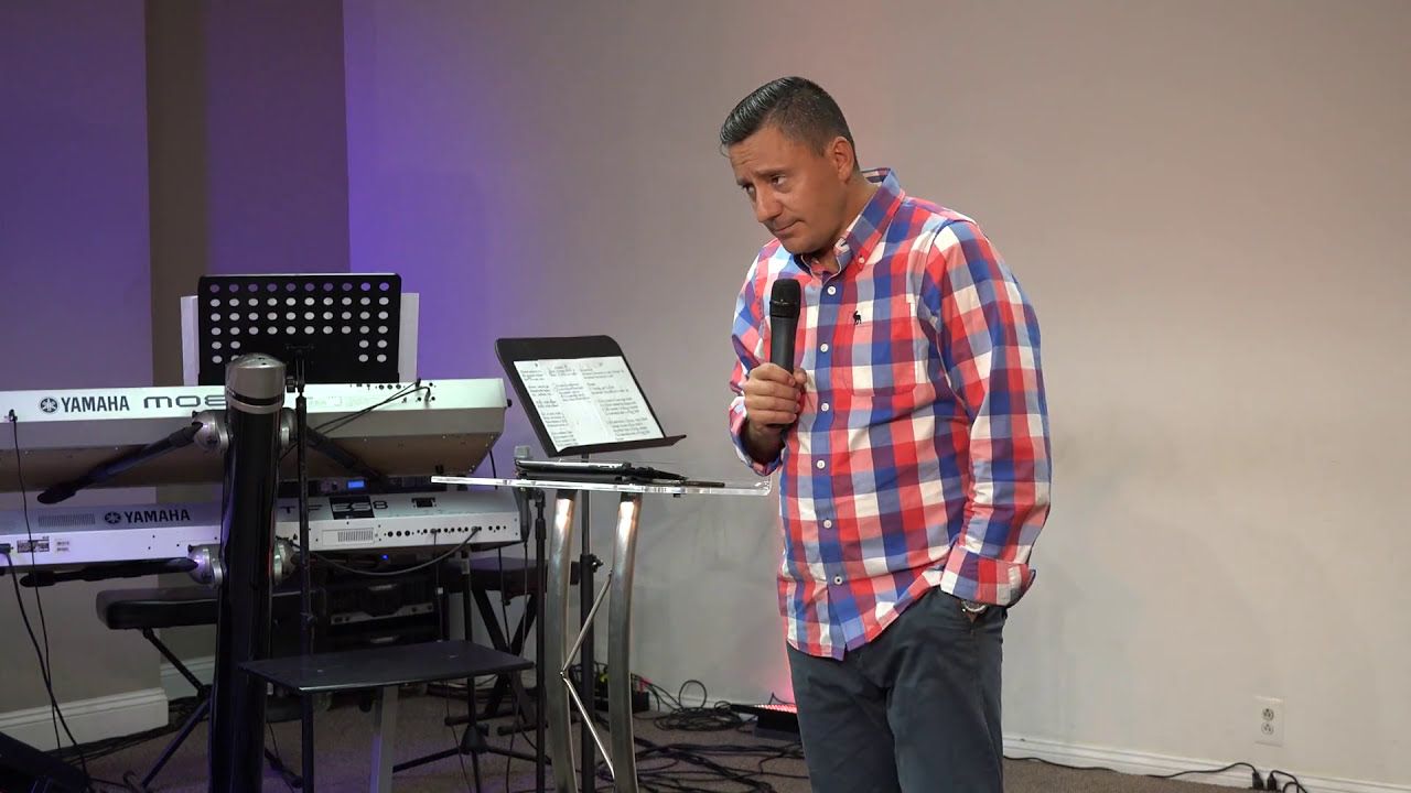 Ruslan Murin in a checked shirt holding a microphone beside a lectern, his head tilted.