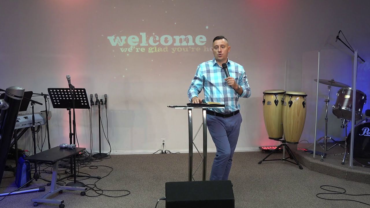 Ruslan Murin preaching into a microphone at a lectern, one hand resting on an open book.