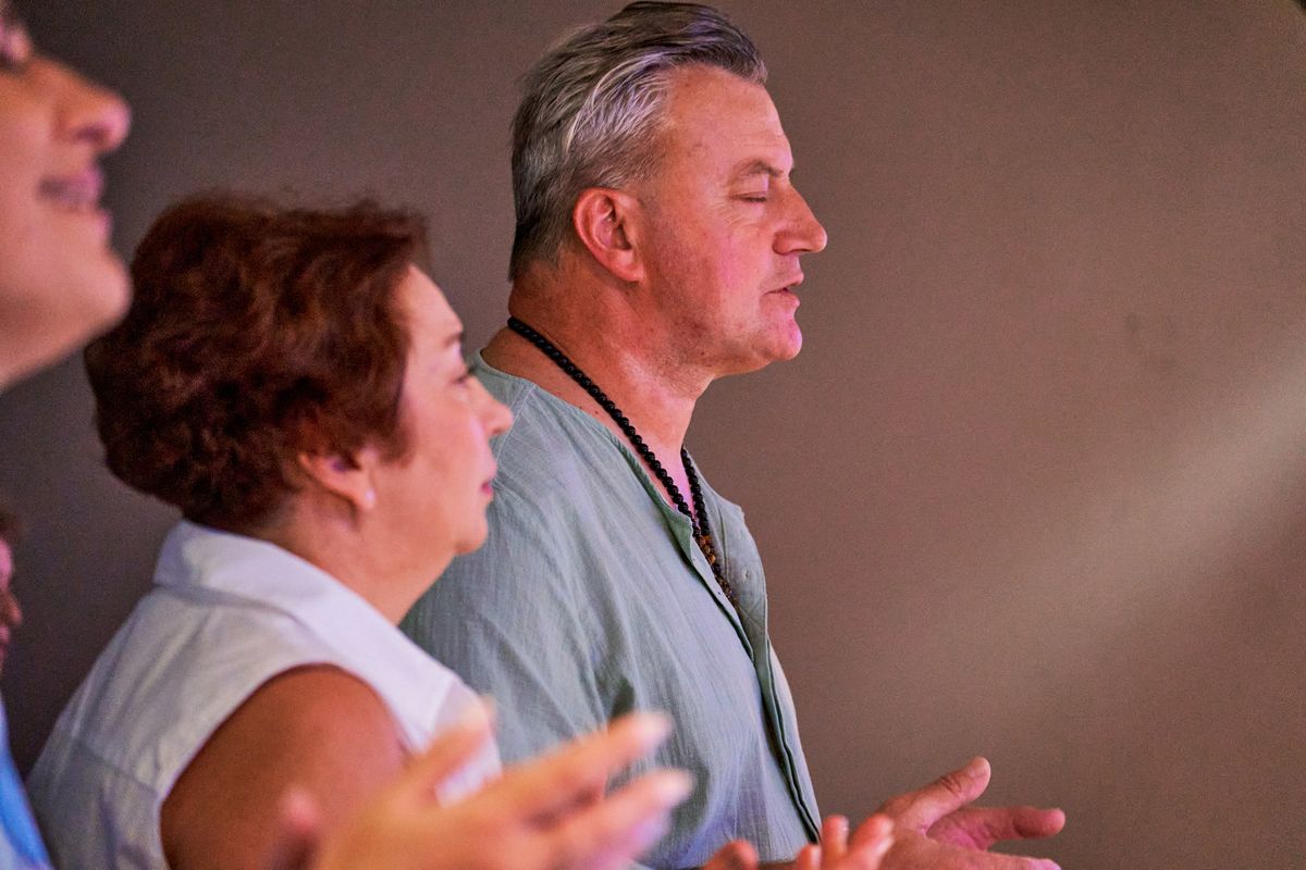 A man in profile with his eyes closed and his hands open in prayer; a woman beside him